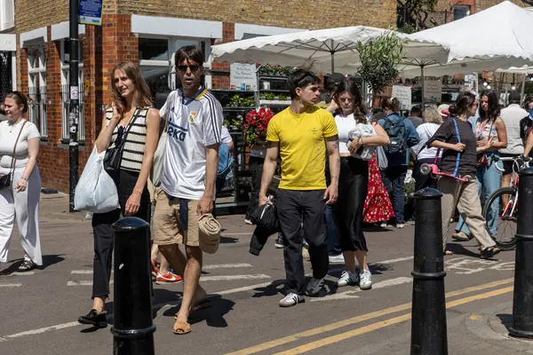 Londra, İngiltere, 5 Mayıs 2025, Pazar tezgahlarıyla güneşli bir sokakta yürüyen insanlar.