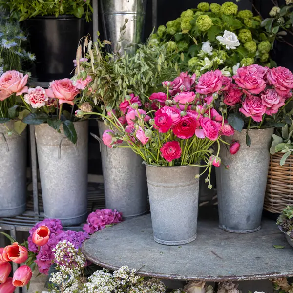 Pembe güller, ranunculus ve metal kovalardaki diğer çiçekler..