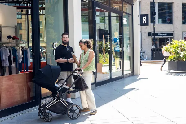 Londra, İngiltere, 5 Mayıs 2025, Güneşli bir günde bebek arabalı bir çift dükkanın önünde dikiliyor..