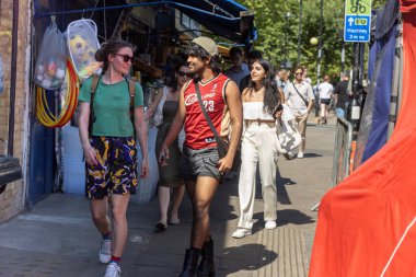 Londra, İngiltere, 5 Mayıs 2025, Yoğun Bir Sokakta Yürüyen Çeşitli İnsanlar. Kırmızı tişörtlü ve şortlu bir adam pazar günü Broadway yolunda yeşil tişörtlü bir kızla yürüyor.