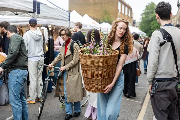 Londra, İngiltere, 7 Mayıs 2025, uzun dalgalı saçlı genç bir kadın, Columbia Çiçek Yolu Pazarı 'ndan alınmış bir sepet çiçek taşıyor.