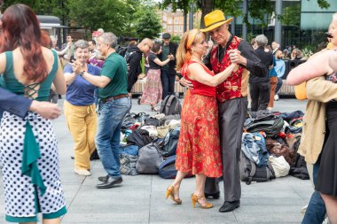 Londra, İngiltere, 15 Mayıs 2025, People Salsa Dancing Outdoor. Kırmızı batılı ve sarı şapkalı adam elbiseli kadınla dans ediyor.
