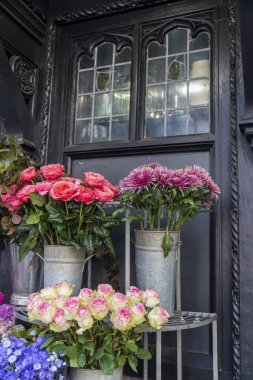 Canlı pembe ve beyaz güller ve metal kovalarda mor kasımpatılar dekoratif bir pencerenin yanında.