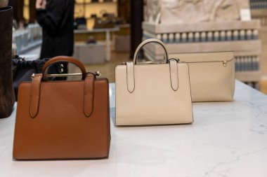Londra, İngiltere, 15 Mayıs 2025, şık bej ve kahverengi deri çantalar bir mağazanın açık renkli mermer yüzeyinde sergileniyor. İskoçya 'da tasarlanan ve İspanya' da el yapımı en kaliteli derileri kullanan çilekli Nano Tote çanta.
