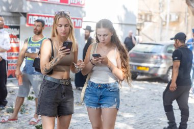 Haifa, Israel, 22 June 2025  Two young girls read the news on their phones against the backdrop of a destroyed sidewalk.  An Iranian missile hits a fountain and a building in the Adar district. The Israeli-Iranian War.