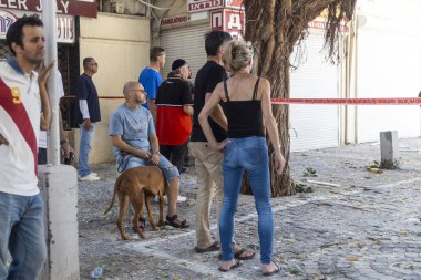 Hayfa, İsrail, 22 Haziran 2025 Halk ve bir köpek kaldırımlı bir şehir sokağında bariyer bantla yıkıntıların temizlenişini izliyorlar bir İran füzesi Adar bölgesinde bir fıskiyeye ve bir binaya çarpıyor. İsrail-İran Savaşı..