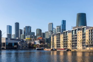 Londra, İngiltere, 12 Mayıs 2025, Canary Wharf A panoramik manzara modern şehir manzarası sayısız yüksek binalar ve belirgin silindirik gökdelen, geniş bir su kütlesi ve demirli tekneler.