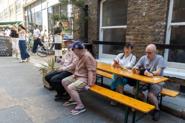 Londra, İngiltere, 12 Mayıs 2025, Londra 'da güneşli bir sokakta açık hava masalarında oturan insanlar..