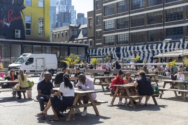 Londra, İngiltere, 12 Mayıs 2025, Londra 'da piknik masaları olan bir açık hava yemekhanesinde insanlar sosyalleşiyor..