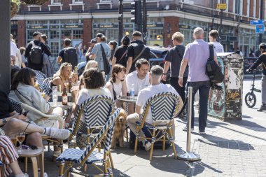 Londra, İngiltere, 12 Mayıs 2025, Bir grup arkadaş ve bir köpek açık bir kafede güneşli bir günün tadını çıkarıyorlar.