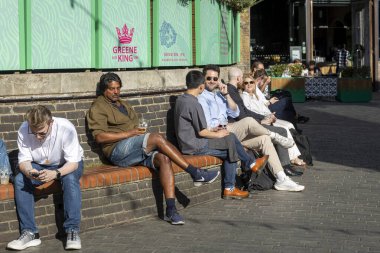 Londra, İngiltere, 7 Mayıs 2025, Güneşli bir günde içeceklerin tadını çıkaran bir grup insan.
