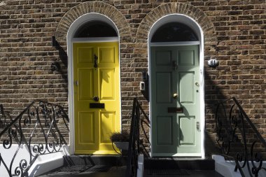 Londra 'da geleneksel tuğla bir evin girişini işaret eden kemerli kırmızı tuğlalı bir çerçeveye sahip büyüleyici mavi bir ön kapı. yemyeşil bitkiler ve canlı kırmızı tırmanma gülleri kapının etrafını süslüyor ve taş basamaklar.