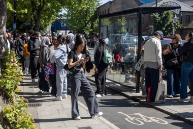 Londra, İngiltere, 11 Mayıs 2025, Camden kasabasındaki otobüs durağı. Genç bir Asyalı kadın kaldırımda dikilirken telefonuna bakar..