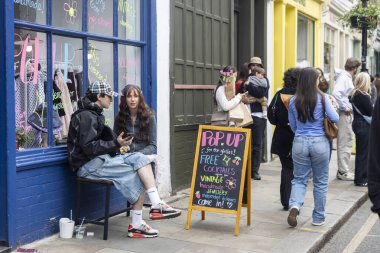 Londra, İngiltere, 9 Mayıs 2025, İnsanlar bir vintage mağazasının önünde rahatlıyor ve alışveriş yapıyor. Çift bankta oturuyor.