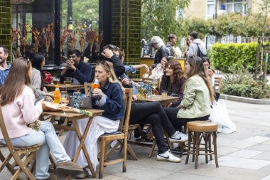 Londra, İngiltere, 9 Mayıs 2025 Bir Outdoor Cafe 'de Sosyalleşen İnsanlar. Çeşitli etnik kökenlere sahip kadın ve erkek çoklu yetişkinler eğleniyorlar..