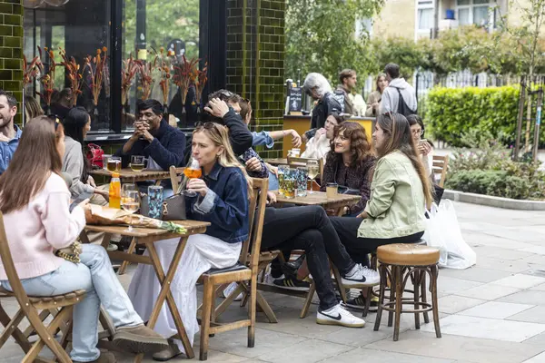 Londra, İngiltere, 9 Mayıs 2025 Bir Outdoor Cafe 'de Sosyalleşen İnsanlar. Çeşitli etnik kökenlere sahip kadın ve erkek çoklu yetişkinler eğleniyorlar..