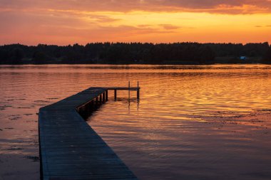 Moskova bölgesindeki bir köyün yakınındaki Rus Volga Nehri 'nde gün batımı. Nehre inen ahşap iskele. Ön planda sazlıklar.