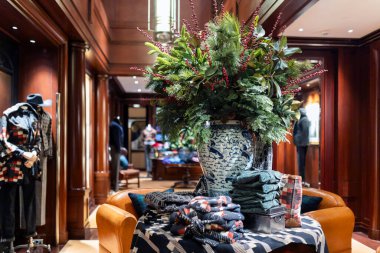 Londra, İngiltere, 24 Kasım 2024. Bir Ralph Lauren mağazasının içinde, her zaman yeşil dalları ve kırmızı böğürtlenleri olan, deri bir kanepede duran mavi ve beyaz bir porselen vazoda büyük bir çiçek aranjmanı var..