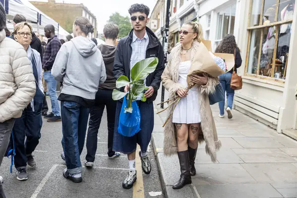 Londra, İngiltere, 5 Mayıs 2025, kalabalık bir açık hava pazarında çiçek ve bitkilerle yürüyen genç çift.