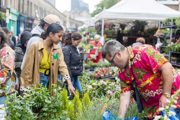 Londra, İngiltere, 11 Mayıs 2025. Kolombiya Yolu Çiçek Pazarı çeşitli tezgahlarda bitki ve çiçekleri keşfeden insanlarla dolup taşıyor..