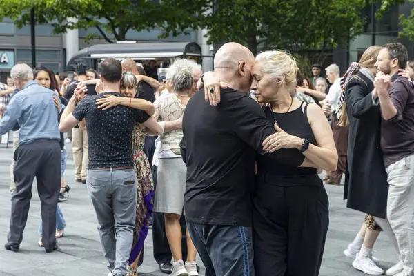 Londra, İngiltere, 11 Mayıs 2025. Çeşitli bir grup insan şehir ortamında tango yapmaktan hoşlanıyor. Odaklanmış, birbirine bağlı ifadelerle yakın dans eden yaşlı bir çift..
