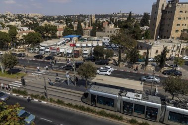 Kudüs, İsrail, 23 Temmuz 2025, şehir binalarıyla çevrili hafif tren, araba ve yayaların olduğu bir sokak sahnesi. Doğu ve Batı Kudüs arasında tramvay hattı boyunca bölünen hattın dibindeki müzenin çatısından bir manzara