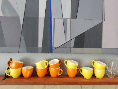 Renkli turuncu ve sarı seramik bardaklar büyük, soyut mecazi bir tablonun arka planında sergileniyor.