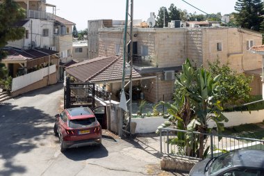 Daliyat al-Karmel, Hayfa, İsrail, 3 Ekim 2025. Akdeniz tarzı bir köyde dar bir yerleşim yerinin parlak, güneşli bir manzarası, kırmızı bir SUV, taş yüzlü evler ve yemyeşil bitkilerin yer aldığı