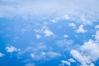 Kabarık beyaz bulutları ve mavi gökyüzünü uçaktan yansıtıyor.