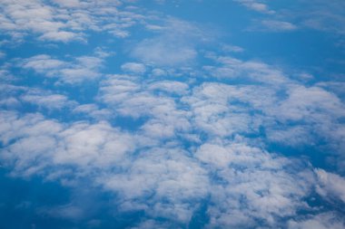Kabarık beyaz bulutları ve mavi gökyüzünü uçaktan yansıtıyor.