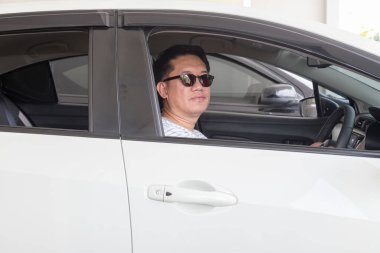 Asyalı bir adam araba kullanıyor ve siyah gözlükler takıyor.