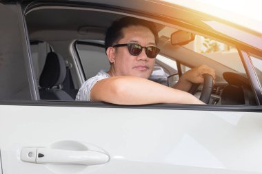 Asyalı bir adam araba kullanıyor ve siyah gözlükler takıyor.