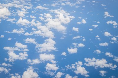 Kabarık beyaz bulutları ve mavi gökyüzünü uçaktan yansıtıyor.