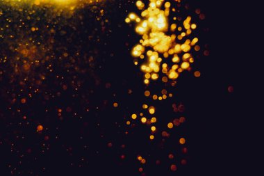 Siyah arkaplanla kutlama yapmak için kullanılan bulanık altın renkli parlak yıldızlar.