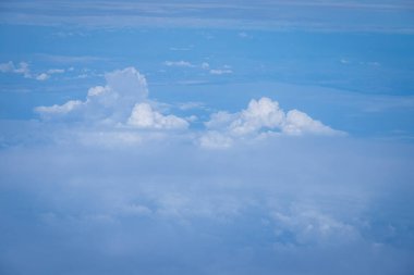 Kabarık beyaz bulutları ve mavi gökyüzünü uçaktan yansıtıyor.