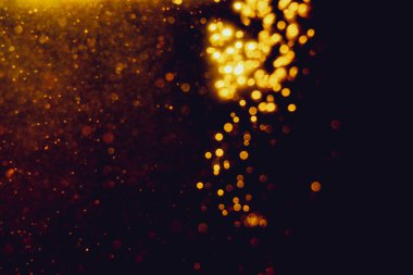 Siyah arkaplanla kutlama yapmak için kullanılan bulanık altın renkli parlak yıldızlar.