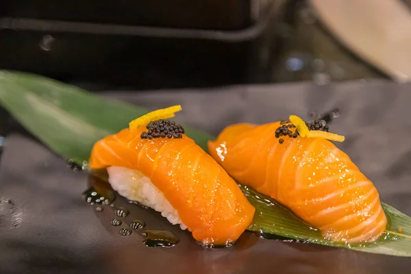 stock image Salmon sushi placed on bamboo leaves in a black plate.