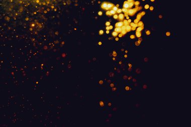 Siyah arkaplanla kutlama yapmak için kullanılan bulanık altın renkli parlak yıldızlar.