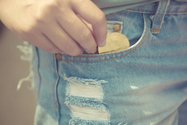 A closeup of a woman putting bitcoin cryptocurrency coin in a blue jeans pocket,Cashless Society concept
