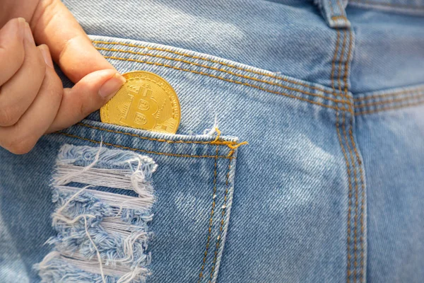 A closeup of a woman putting bitcoin cryptocurrency coin in a blue jeans pocket