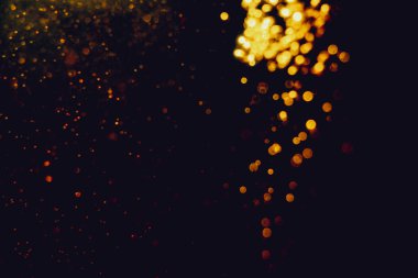 Siyah arkaplanla kutlama yapmak için kullanılan bulanık altın renkli parlak yıldızlar.