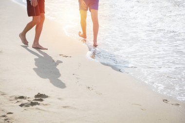 İki arkadaş sahilde rahatça yürüyor ve sahilde ayak izleri var.