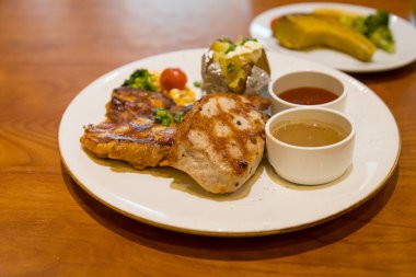 Izgara domuz bifteği, patates püresi ve sebzeyle servis edilir.