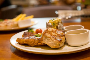 Izgara domuz bifteği, patates püresi ve sebzeyle servis edilir.