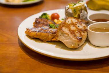 Izgara domuz bifteği, patates püresi ve sebzeyle servis edilir.