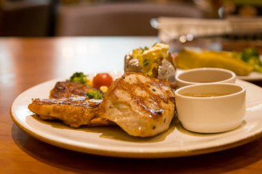 Izgara domuz bifteği, patates püresi ve sebzeyle servis edilir.