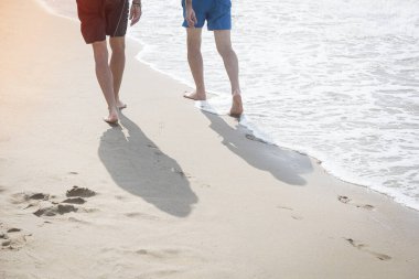 İki arkadaş sahilde rahatça yürüyor ve sahilde ayak izleri var.