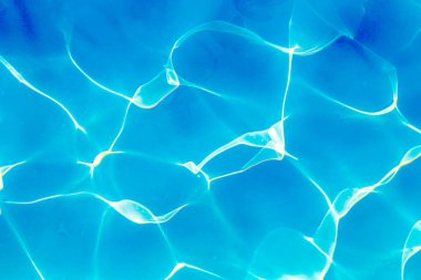 Parlak güneş ışığı yansımalarıyla canlı mavi yüzme havuzu suyunun yakın çekimi dinamik desenler oluşturur.