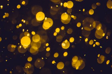 Koyu bir arka planda farklı boyut ve renklerde odanmamış altın bokeh ışıkları.