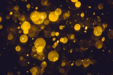 Koyu bir arka planda farklı boyut ve renklerde odanmamış altın bokeh ışıkları.